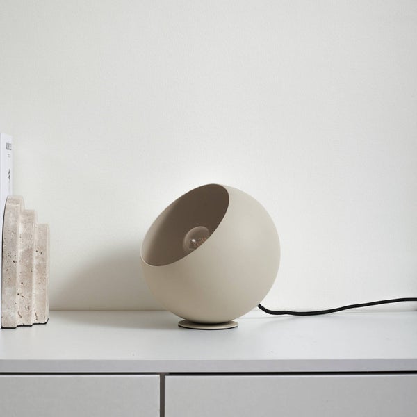 Kugelförmige Tischleuchte in Beige mit mattem Finish, sichtbarem Leuchtmittel und schwarzem Stromkabel.