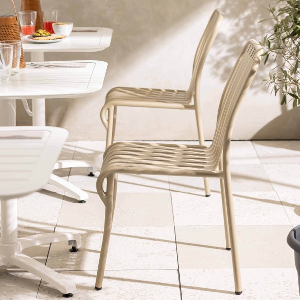 Moderne Gartenstühle aus Metall in Beige mit Streben-Design an einem weißen Bistrotisch auf einer hellen Terrasse.
