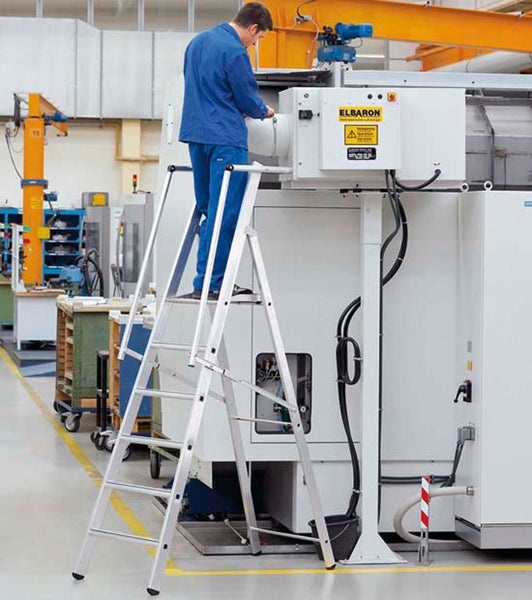 Mann auf einer Aluminiumleiter, der an einer Maschine arbeitet, in einer Werkshalle