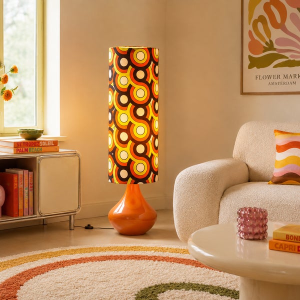 Eine zylindrische Stehlampe mit Retro Muster in einem hellen Wohnzimmer mit Couch und Beistelltisch.