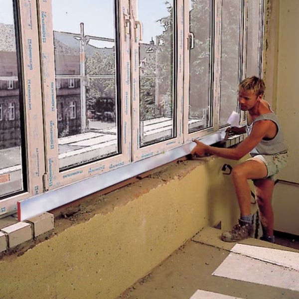 Handwerker richtet Fensterbank mit Wasserwaage unter einem eingebauten Kunststofffenster aus.