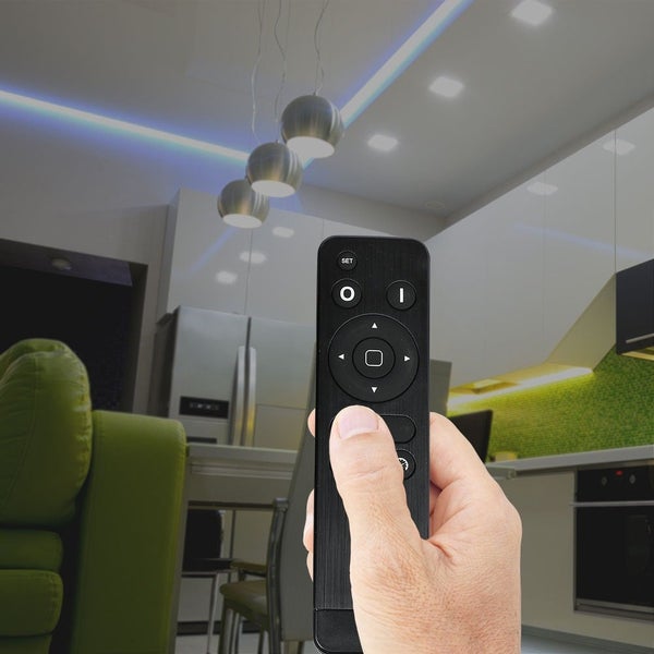 Eine Hand hält eine Fernbedienung in einem Wohnzimmer, zur Steuerung von Lampen und Beleuchtung