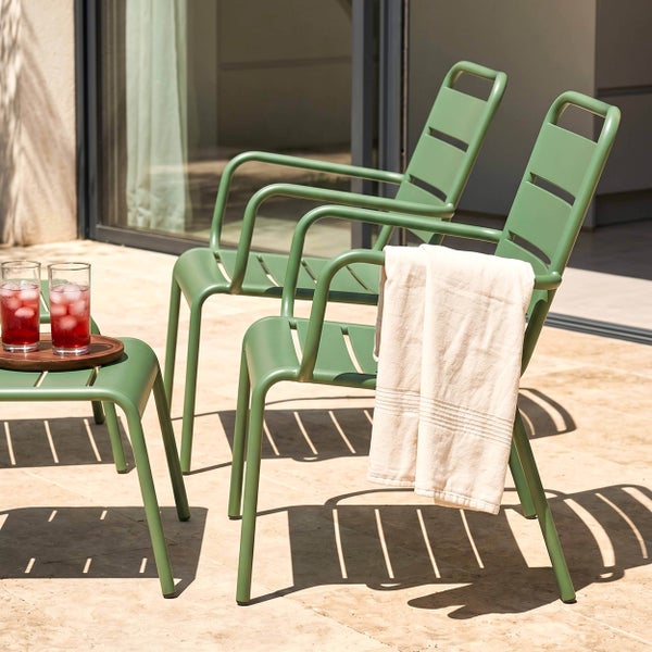 Zwei grüne Gartenstühle aus Metall mit Armlehnen und ein Beistelltisch auf einer sonnigen Terrasse. Ein helles Handtuch hängt über einem Stuhl.