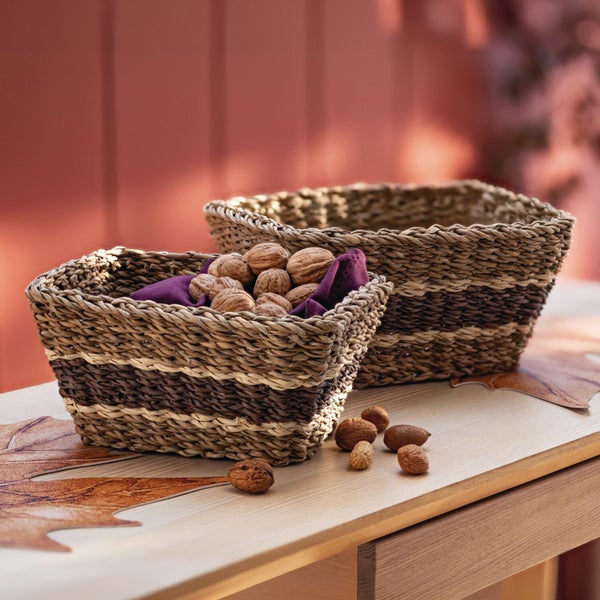 Zwei rechteckige geflochtene Aufbewahrungskörbe aus Naturmaterial stehen auf einem Holztisch, gefüllt mit Nüssen.