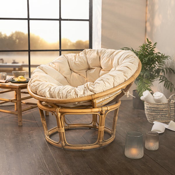 Szene mit einem Papasansessel aus Rattan mit beigem Kissen in einem hellen Raum.