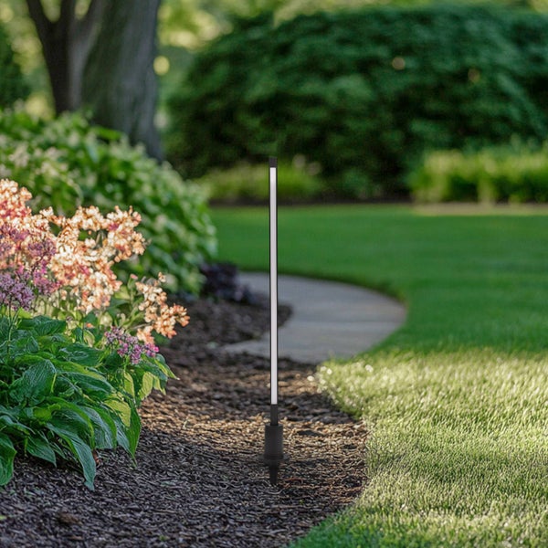 Schlanke schwarze LED Gartenleuchte in einem Blumenbeet neben einer Rasenfläche und einem Gartenweg.