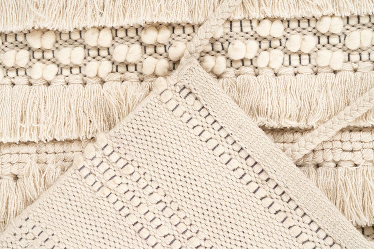 Detailaufnahme eines gewebten Teppichs in Beige mit Fransen, Noppen und Flechtmustern.