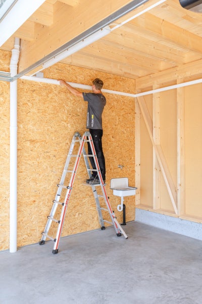 Mann auf einer Leiter in einem Raum mit Holzverkleidung, der eine Lichtleiste anbringt