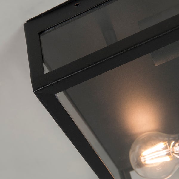 Nahaufnahme einer schwarzen Außenleuchte aus Metall und Glas mit leuchtendem Filament-Leuchtmittel.