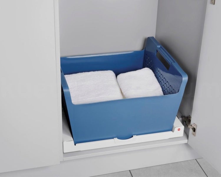 Blauer Aufbewahrungskorb aus Kunststoff mit weißen Handtüchern auf einem Auszugsboden in einem weißen Schrank.