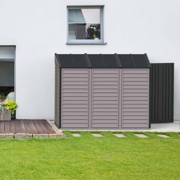 Moderner Gartenschrank mit drei Türen und dunklem Pultdach, platziert an einer weißen Hauswand neben Rasen und Holzterrasse.