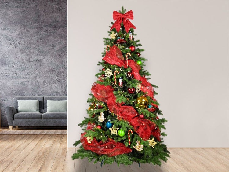 Geschmückter künstlicher Weihnachtsbaum mit roter Schleife und Dekoration im Wohnzimmer.