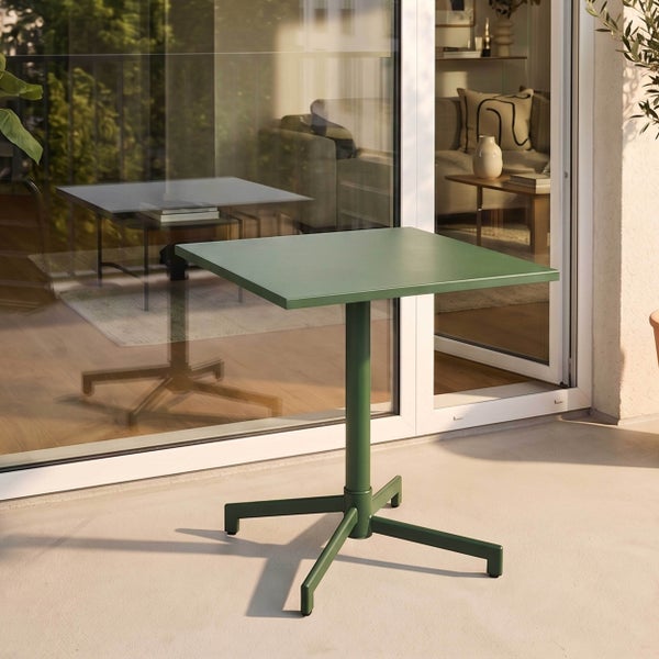 Quadratischer, grüner Bistrotisch aus Metall auf einem hellen, sonnigen Balkon vor einer Glastür.