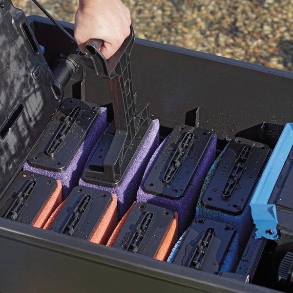 Hand zieht am Reinigungsgriff eines Teichfilterschwamms in einem schwarzen Filtergehäuse mit mehreren Filterschwämmen.