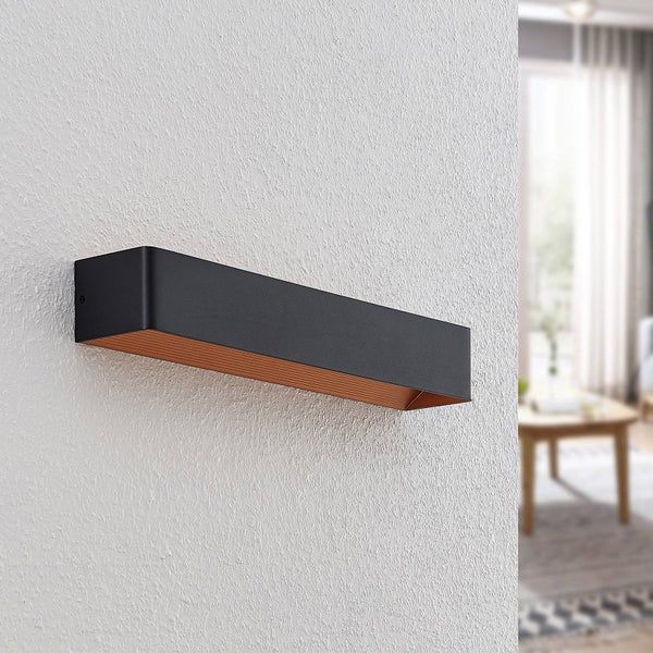 Moderne rechteckige Wandleuchte in Schwarz mit kupferfarbener Innenseite an einer Wand in einem hellen Wohnzimmer.