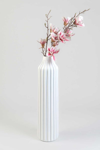 Hohe, schlanke Vase aus Keramik mit vertikaler Rillenstruktur und künstlichen Magnolienzweigen.