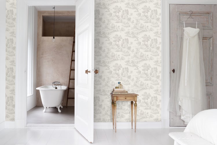 Hell gestalteter Raum mit Toile-de-Jouy Vliestapete, Blick ins Badezimmer mit freistehender Badewanne und hölzernem Beistelltisch.