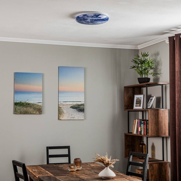 Deckenleuchte mit blauem Marmormuster in einem hellen Esszimmer mit Holztisch, Wandbildern und einem Holzregal.
