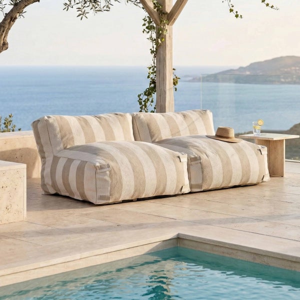 Modernes, gestreiftes Outdoor-Lounge-Sofa auf einer hellen Steinterrasse am Pool mit Blick auf das Meer.