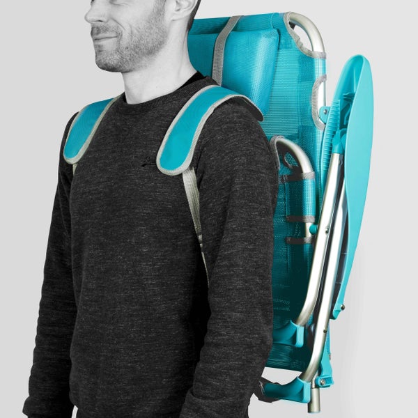 Zusammenklappbarer Strandstuhl in Türkis mit Rucksackgurten, der von einer Person auf dem Rücken getragen wird.