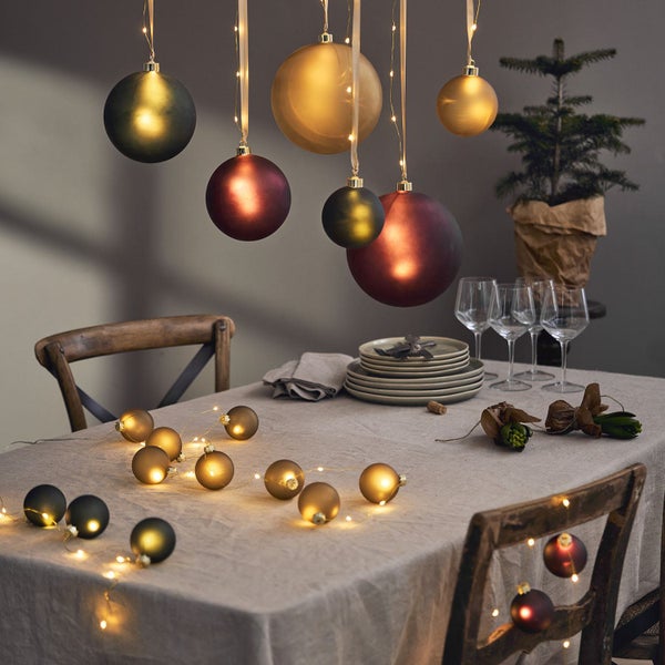 Festliche Tischdekoration mit Weihnachtskugeln und Lichterkette für eine gemütliche Atmosphäre.