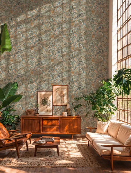 Wohnzimmer mit Vliestapete im botanischen Muster hinter einem Holzsideboard, ergänzt durch Zimmerpflanzen, Ledersessel und ein helles Sofa.