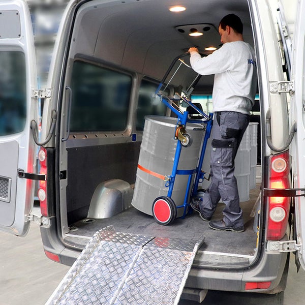 Eine Person lädt ein Fass mit einem Fasswagen über eine Laderampe aus Metall in einen Transporter.