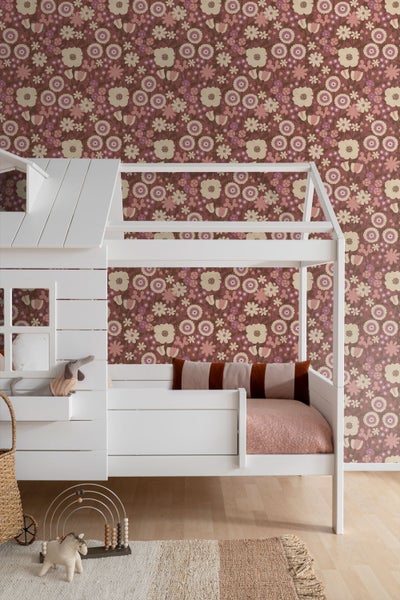 Kinderzimmer mit weißem Hausbett vor einer Wand mit floraler Tapete in Rosa und Beige.