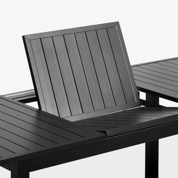 Rechteckiger, dunkelgrauer Ausziehtisch aus Aluminium auf einer Holzterrasse vor einer Glasfront mit grünen Pflanzen.