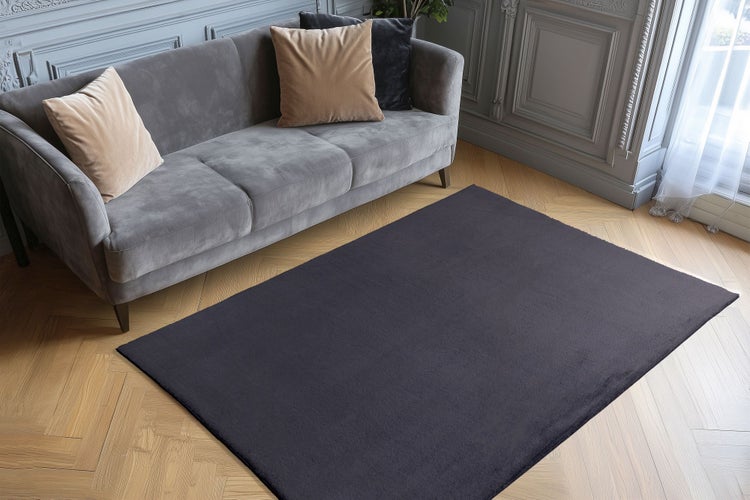 Ein rechteckiger Teppich vor einem Sofa auf einem Parkettboden in einem elegant eingerichteten Wohnzimmer.