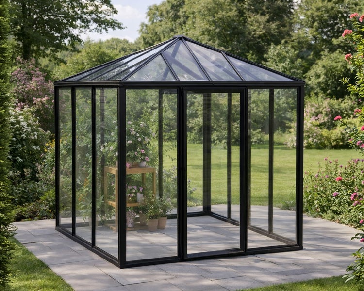 Modernes, quadratisches Gewächshaus mit schwarzem Metallrahmen und Glaseinsätzen auf einer Steinterrasse in einem hellen, gepflegten Garten.