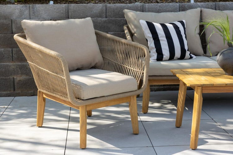 Moderner Loungesessel mit Holzgestell und beigem Seilgeflecht, inklusive Polstern, auf einer gepflasterten Terrasse.