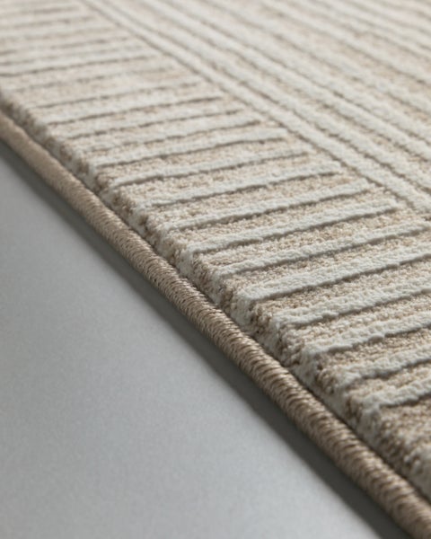 Nahaufnahme eines beige gestreiften Teppichs mit strukturierter Oberfläche und geketteltem Rand.