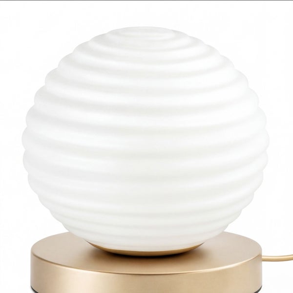 Moderne Tischleuchte mit kugelförmigem, geriffeltem Schirm aus weißem Glas und rundem Metallfuß in Goldoptik.