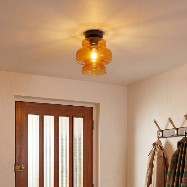 Moderne Deckenleuchte mit bernsteinfarbenem Glasschirm im Flur, montiert an einer hellen Zimmerdecke über einer Holztür mit Garderobe.