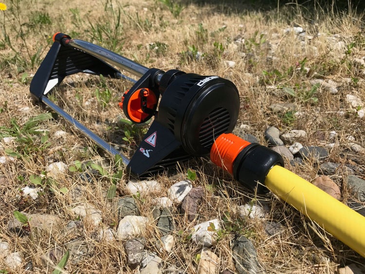 Claber Viereckregner auf einer Rasenfläche, angeschlossen an einen Gartenschlauch, mit Metalldüsenrohr und Gehäuse aus Kunststoff.