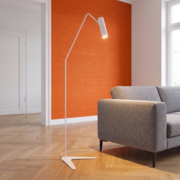 Moderne, schlanke Stehleuchte mit gewinkeltem Arm und zylindrischem Kopf neben einem grauen Sofa in einem hellen Wohnzimmer.