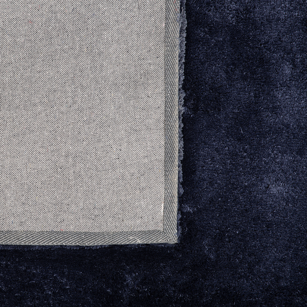Nahaufnahme eines dunkelblauen Hochflor-Teppichs mit gewebtem Textilrücken und verstärktem Rand.
