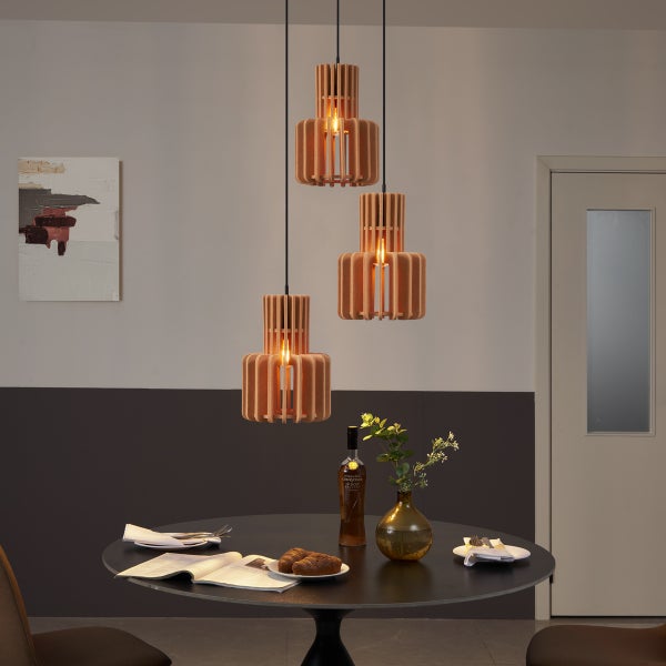 Moderne dreiflammige Pendelleuchte mit abgestuften Schirmen aus vertikalen Holzlamellen, die über einem runden schwarzen Esstisch hängen.