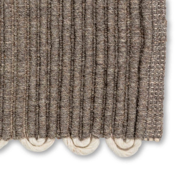 Nahaufnahme eines gewebten Teppichs mit vertikaler Rippstruktur und dekorativen Schlaufen am Rand.