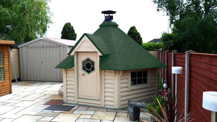 Gartensauna mit Holzwänden und grünem Dach auf einer gepflasterten Fläche