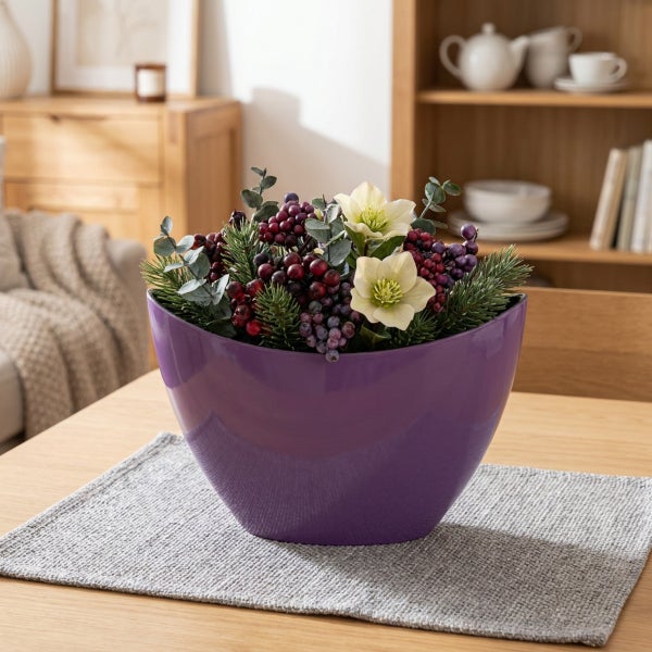 Dekorative Pflanzschale mit künstlichem Blumengesteck aus Beeren, Tannenzweigen und Blüten in einem Wohnraum auf einem Holztisch.