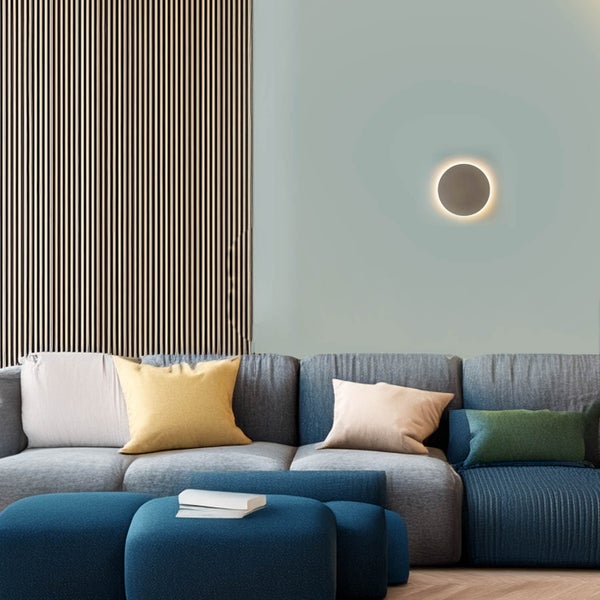 Wohnzimmer mit grauem Sofa, blauen Hockern, Wandleuchte und Holzpaneel