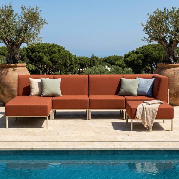 Modulares Garten-Lounge-Set aus rostfarbenem Stoff auf einer Terrasse am Pool mit Zierkissen und zwei Olivenbäumen im Hintergrund.