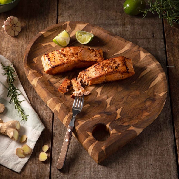 Zwei Lachsfilets auf einem Holzbrett mit Limetten und einem Stück Ingwer.
