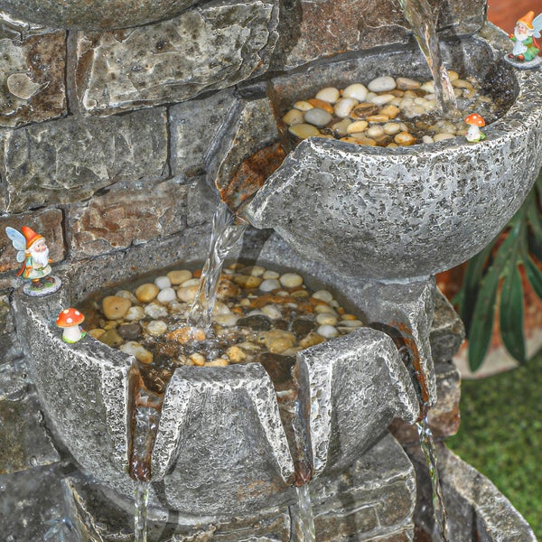 Beleuchteter Kaskadenbrunnen in Steinoptik auf einer Terrasse neben einem Hauseingang und Blumenkübeln.
