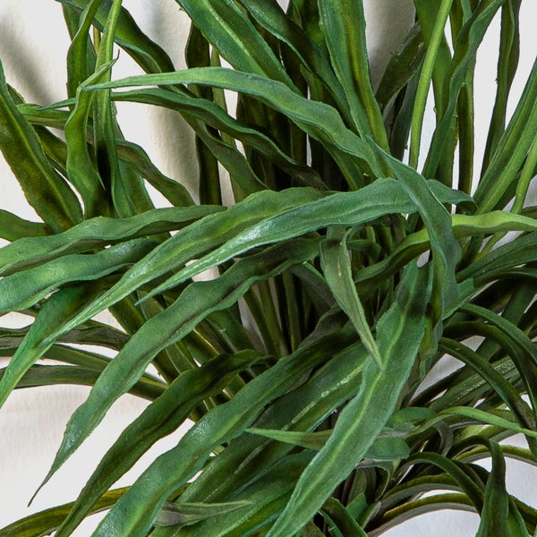 Künstliche Pflanze mit langen, gewellten grünen Blättern aus Kunststoff.