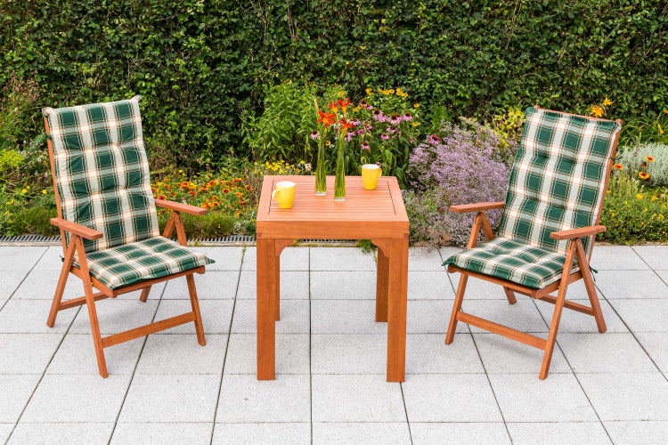 Gartenszene mit zwei Holzstühlen, karierten Auflagen und einem Holztisch mit Blumenvasen und Tassen