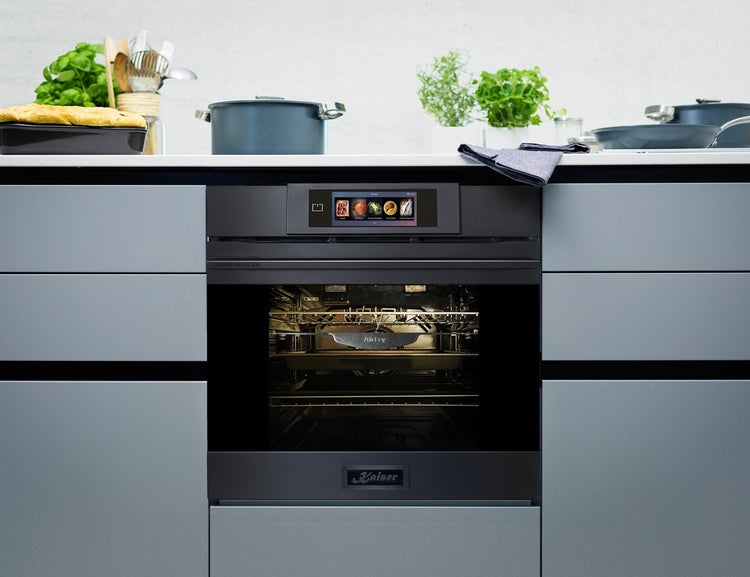 Einbau Backofen mit Touch Display eingebaut in moderne Küchenzeile mit Kochutensilien und Pflanzen auf der Arbeitsplatte.