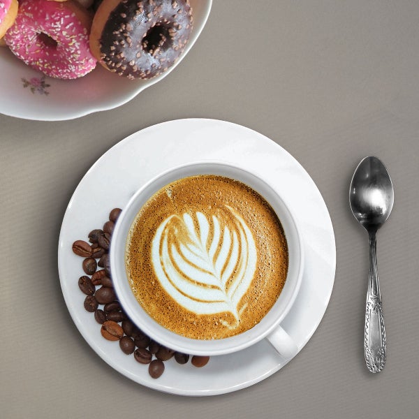 Draufsicht auf eine Tasse Kaffee mit Latte Art, Kaffeebohnen, einen Löffel und Donuts